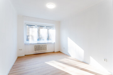 Empty room with wooden floor and white walls receiving sunlight from window