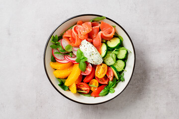 Salmon bowl with spinach,arugula, cherry tomatoes, cucumber, orange slices, radish and cream cheese.  Concept for a tasty and healthy meal. Light gray stone background. Top view.