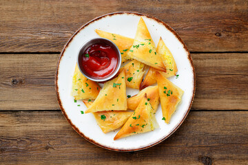 Vegetarian samsa (samosas) with tomato sauce and herbs. Stuffed with potato. on wooden  background, top view	