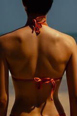 Female in bikini at beach with blue sky and ocean backdrop. Skin care, sun protection