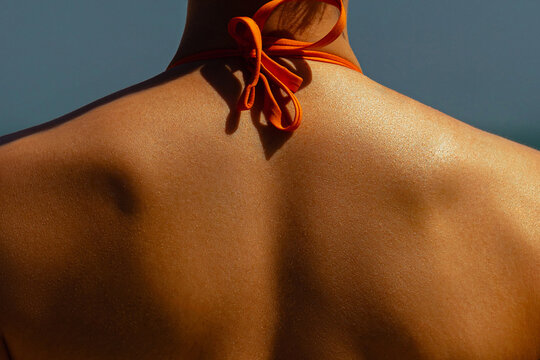 Female back in orange bikini under sunlight. Skin care, sun protection