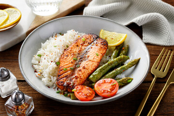 Baked salmon fish steak with asparagus fried rice and lemon slice. Delicious lunch or dinner for every day. Wooden background