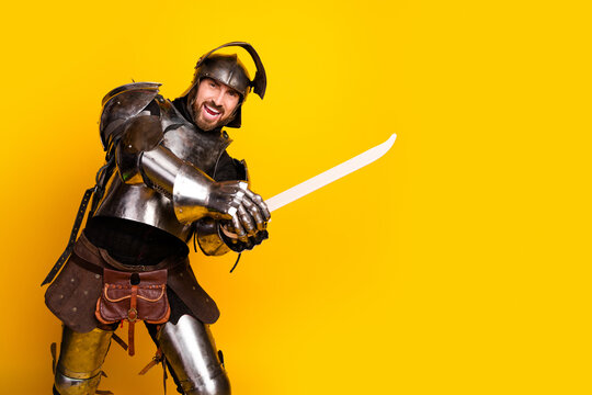 Young man dressed as a medieval knight posing with a sword in front of a vibrant yellow background for a themed costume event