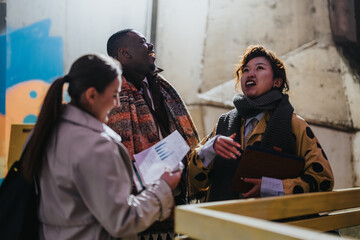 Three people of diverse backgrounds engaging in a conversation in an outdoor urban setting, sharing documents and enjoying their interaction during a collaborative discussion.