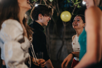 A group of friends enjoy laughter and conversation during an outdoor celebration at night. String lights and ambient surroundings add to the joyous mood of the gathering.