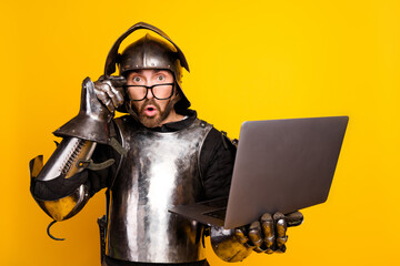 Young man in medieval knight armor using a laptop against vibrant yellow background