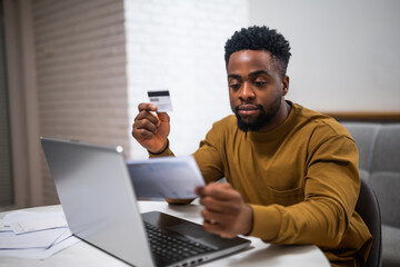 Modern young black man using credit card and laptop at home. He is focusing on e-commerce and managing his finances.