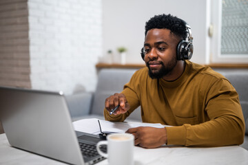 Modern young African-American man using wireless headphones and laptop while participating in e-learning session from the comfort of his home.