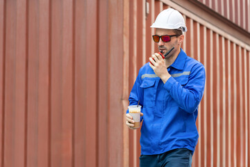 Engineer man walking at shipping yard, Warehouse worker using walkie talkie and talking about work in cargo containers