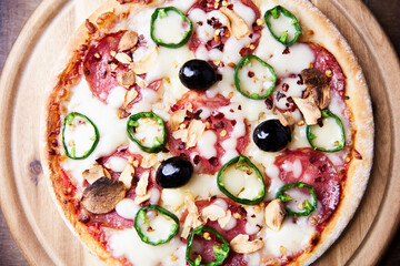 Pizza with salami and mozzarella cheese, jalapeno pepper and black olives. Wooden background. Soft focus. Top view. Close up.