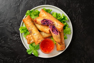 Fresh fried spring rolls stuffed with red cabbage and carrot served with sweet chili dip sauce. Black background, top view.