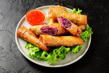 Fresh fried spring rolls stuffed with red cabbage and carrot served with sweet chili dip sauce. Black background