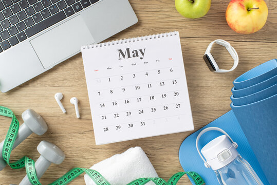 A calendar alongside fitness accessories like weights, smartwatch, yoga mat, and measuring tape on a wooden desk