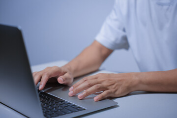 Cropped shot of young businessman hand typing on laptop computer while working in white modern office room.