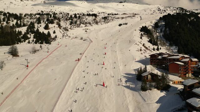 drone video of French luxury ski resort Courchevel in European Alps with ski slope and people skiing at it with wooden mountain hotels nearby  