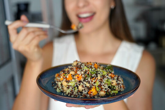 Young woman eating a warm quinoa salad with carrots, broccoli and chickpeas. Focus on the plate.