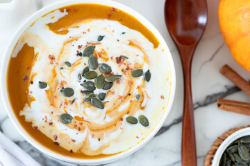 Homemade pumpkin soup with seeds and coconut milk on white marble table with wooden spoon. Top view. Close-up.