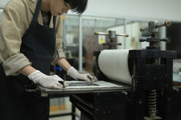 A close-up of a dedicated printmaker carefully positioning an inked plate on the printing press,...