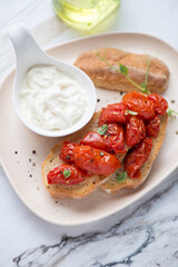 Beige plate with roasted tomato bruschettas and stracciatella cheese, vertical shot on a white granite surface, middle closeup