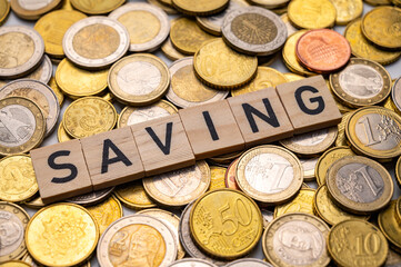 Wooden squares spelling out the word Saving, on top of a surface of euro coins.