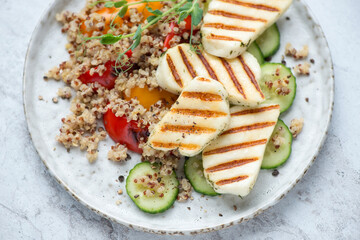 Grilled halloumi cheese with quinoa, bell peppers and cucumber on a grey plate, horizontal shot, middle closeup