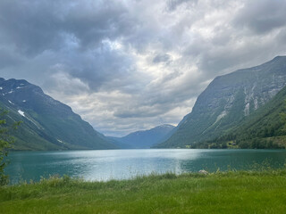 Obraz premium A calm turquoise fjord framed by steep, green mountains under a cloudy sky. The reflective water creates a peaceful, majestic atmosphere.