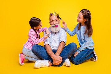 Happy elderly man enjoying playful bonding with granddaughters against yellow background