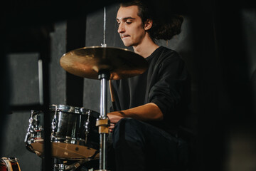 The image depicts a young man playing the drums enthusiastically during a rehearsal in a studio setting, showcasing the dedication and emotion of live musical performance.