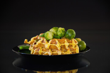 Vegetarian waffles with vegetables on a black plate, isolated on a black background