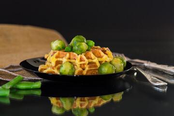 Vegetarian waffles with vegetables on a black plate, isolated on a black background