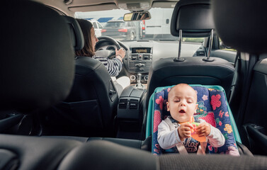 Portrait of laughing baby in car seat while Mother driving a passenger car. Scene captures moment...