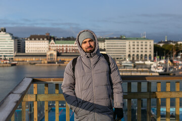 Cropped view of a young adult bearded traveler man in grey puffer coat and grey hat with backpack...