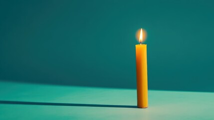 Tall yellow candle burns brightly against a teal background, casting a soft glow and creating delicate shadows during a quiet evening