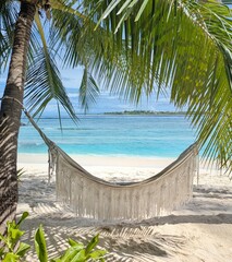 A hammock swings between palm trees on a pristine Maldives beach, offering ultimate relaxation