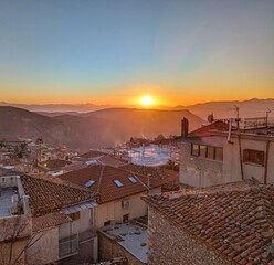 A stunning panoramic view over the mountain town of Arachova, Greece, at sunset, with glowing rooftops and rolling hills