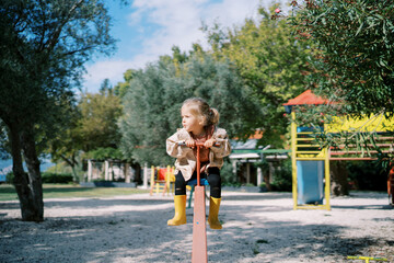Little girl sits on a swing balancer holding the handle and looks to the side