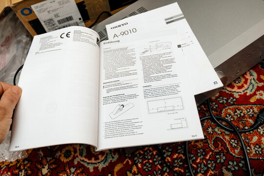 Paris, France - Dec 12, 2022: A person flips through the German-language user manual for the Onkyo A-9010 integrated amplifier, showing technical specifications, installation guides