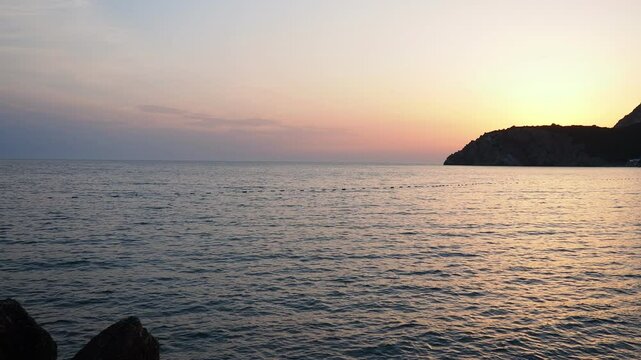 Waves gently lap at shore during stunning sunset over ocean. Sunlight reflects off waves as they roll onto shore, creating tranquil atmosphere at sunset by sea. Montenegro summer. Canj, Bar district