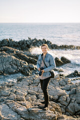 Obraz premium Smiling photographer with a digital camera in his hands stands on a rocky seashore