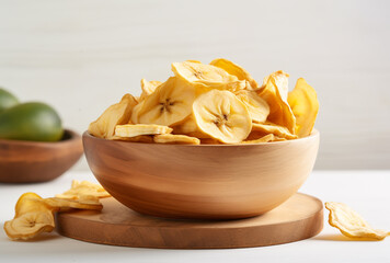 Freshly made banana chips in a wooden bowl on a clean white table