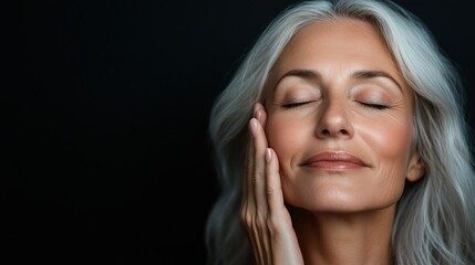 A middle-aged woman touching her face with one hand, showing smooth skin and closed eyes against a black background.