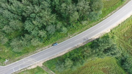 A lonely standing car on a tarmac road through a forest. Vertical view down to the motorway, autobahn in the suburbs.