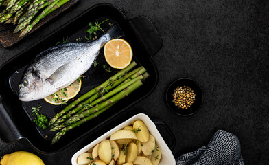 the concept of a delicious dinner. raw dorado fish with asparagus and lemon on dark background.