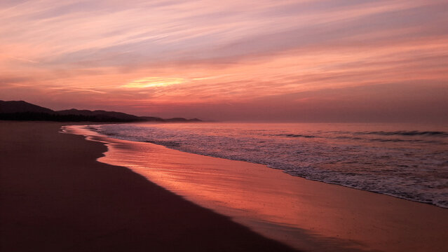 amanecer o atardecer en una playa con olas y brisas con cielo rojizo, nubescoloridas y agua de mar reflejando el cielo