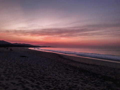 amanecer o atardecer en una playa con olas y brisas con cielo rojizo, nubescoloridas y agua de mar reflejando el cielo