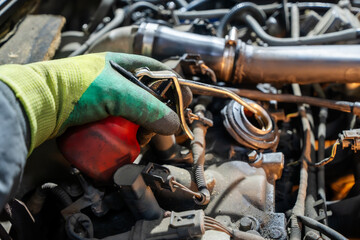 A mechanic's gloved hand using an oil can to lubricate engine components in a car repair shop....