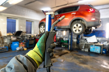 Fototapeta premium A mechanic's gloved hand holding a welding torch in an auto repair shop with a lifted red SUV in the background. Professional vehicle maintenance.