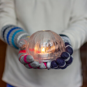 Gloved Hands Holding an Ice Lantern with candle in front of a window.