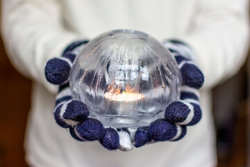 Gloved Hands Holding an Ice Lantern with candle in front of a window.