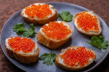Canapes with red caviar on a plate decorated with cilantro on a brown tablecloth